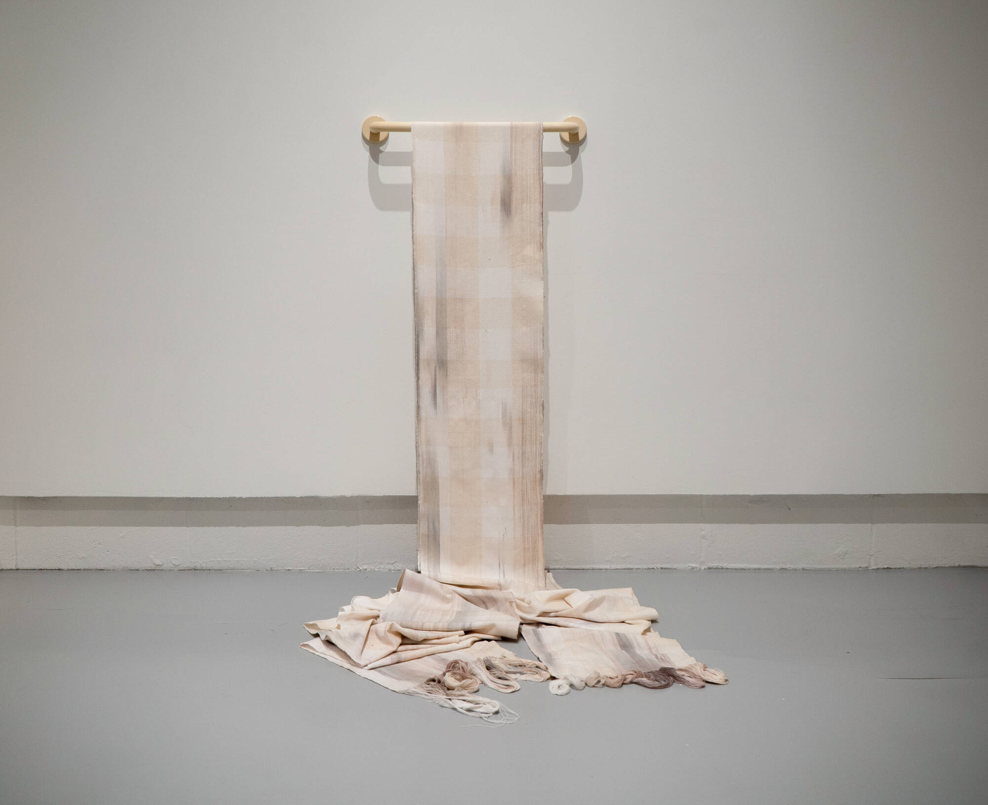 A photograph of a towel bar attached to the wall with a soiled towel that extends to the ground in a pile